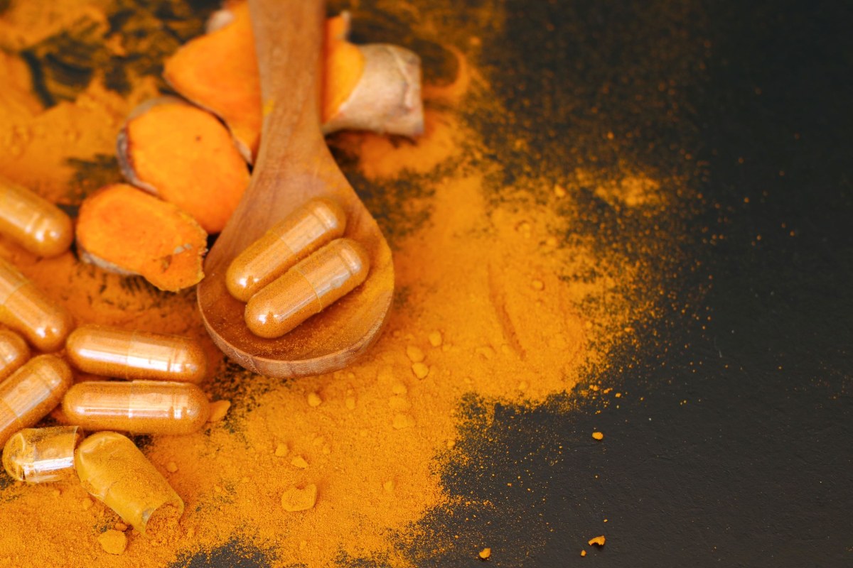 Comparison of turmeric powder in a spoon and turmeric capsules on a table