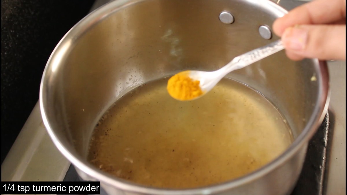 A small bowl of turmeric powder on a kitchen counter next to a cup of tea and a notebook.